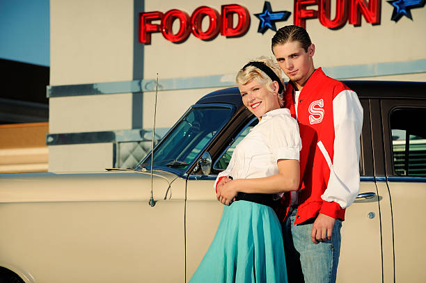 ретро 50-х годов пара стоя возле старый автомобиль и diner - 1950s style couple old fashioned heterosexual couple стоковые фото и изображения