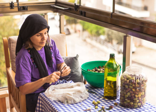 Mature women in home kitchen preparing mix vegetable for salad - cucumber, tomato, olive, lemon, onion.