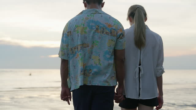 Young couple walking on the beach at sunset.