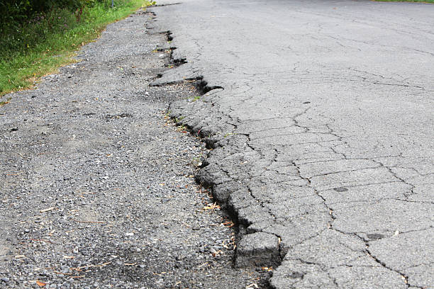 Road Asphalt Cracked Close Up at Edge of Rural Highway Close up of cracked and broken asphalt - with plant debris and scattered, strewn gravel along the edge of a rural road. Portrays the inevitable result of constant traffic and diverse weather combined with delayed, avoided or unaffordable municipal highway maintenance and repair. grass shoulder stock pictures, royalty-free photos & images