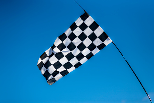 A black and white racing flag is ready to flag the winner against a clear blue sky. Adobge RGB 1998 profile.
