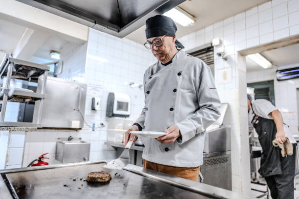 istock Senior chef preparing a hamburger in a commercial kitchen 1830612178