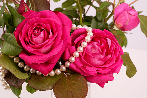 a bouquet of various red roses with green leaves in a vase and a pearl necklace symbolizing a marriage