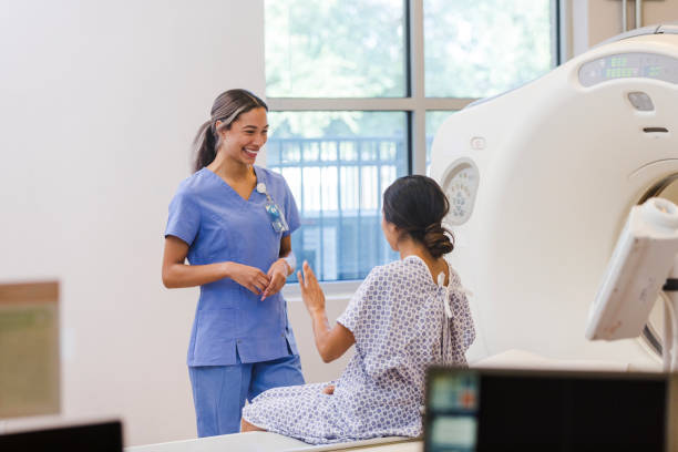 Female CAT technician smiles as unrecognizable female patient speaks The young adult female CT tech smiles and laughs when her unrecognizable female patient tells her a funny story. digital xray stock pictures, royalty-free photos & images