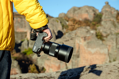 Close-up shot of a photographer holding camera standing on the mountain.