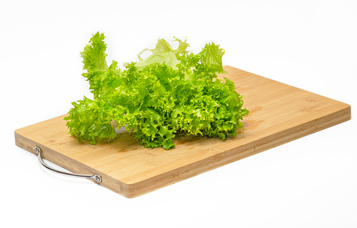 Green salad leaves on wooden cutting board. Side view. Preparing salad for snack.