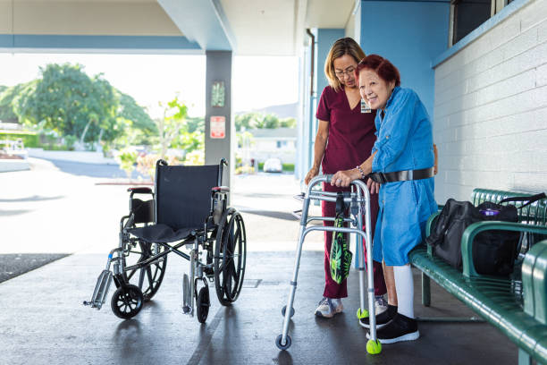 istock Home caregiver assisting elderly patient with transfer gait belt while walking outside medical complex 1830638353