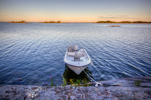 A small motorboat tied up to a rock on a lake in Sweden at dusk.