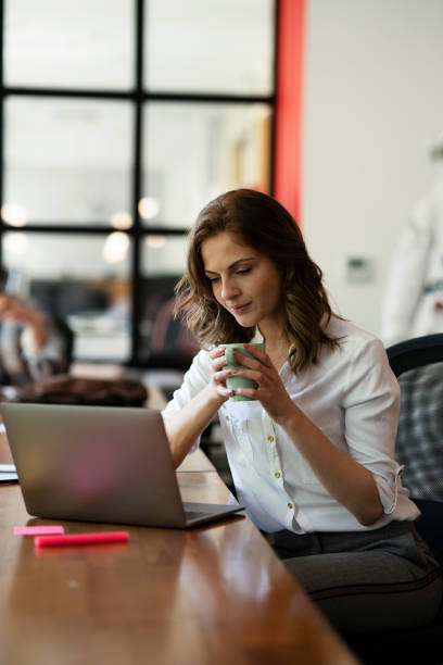 istock Beautiful woman drinking coffee while working on laptop. 1830643156
