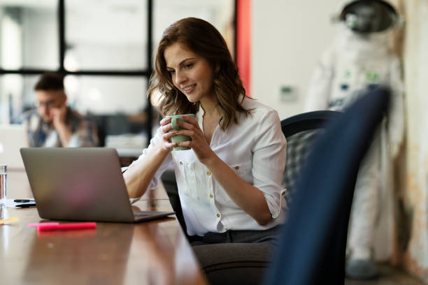 istock Beautiful woman drinking coffee while working on laptop. 1830643723