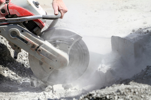 Close-up shot of a cut off saw in action cutting away a section of concrete curb on a road repair project.