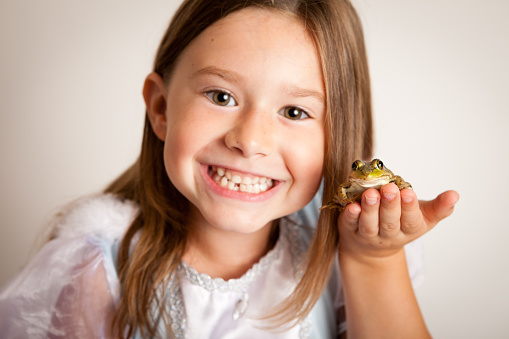 Color photo of a happy, young princess girl holding a frog. Could it be her prince? NOTE: Focus is on the frog.
