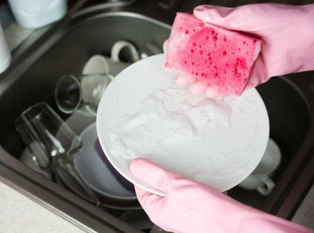istock Woman's hands in rubber gloves hold a soapy kitchen sponge and a plate. Close-up. Selective focus. 1830654633
