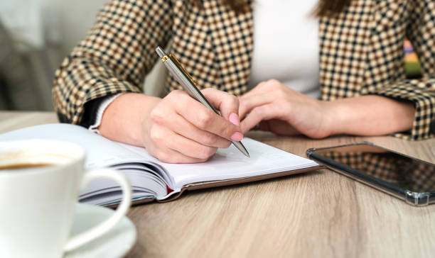 istock A young woman writes writing something in a notepad while sitting in a cafe. Close-up. Selective focus. 1830657888