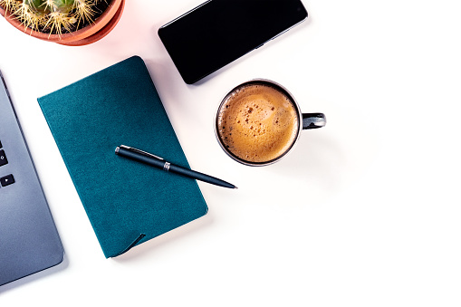 Top view knolling concept at a desktop with open laptop in the center of the frame, with a tablet and a smartphone. Green plant in the corner, Coffee with latte art, and glasses. Scene is white, brightly lit, with white wood on a desktop. Horizontal composition. All screens are white for easier design placement.