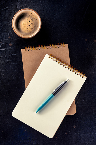 Notebook mockup with a pen and a cup of coffee, top shot on a black background