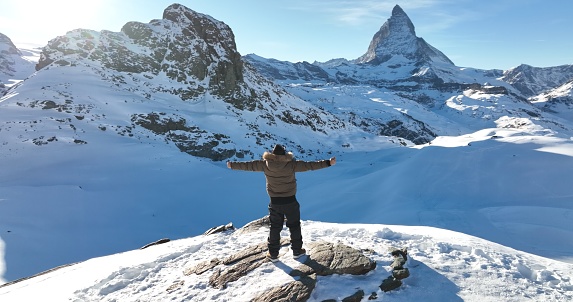 Panoramic landscape of Successful asian man celebrate and raising arms on mountain peak view point with iconic famous Matterhorn background. Swiss alps, Switzerland. Travel and Adventure concept.