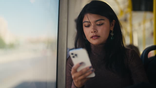 Multi-racial young woman using her mobile smart phone on bus in city