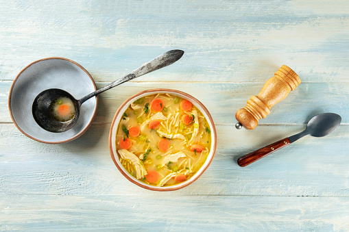 Chicken noodle soup with vegetables, a bowl of healthy broth, overhead flat lay shot on a rustic wooden table, winter home cooking, with copy space