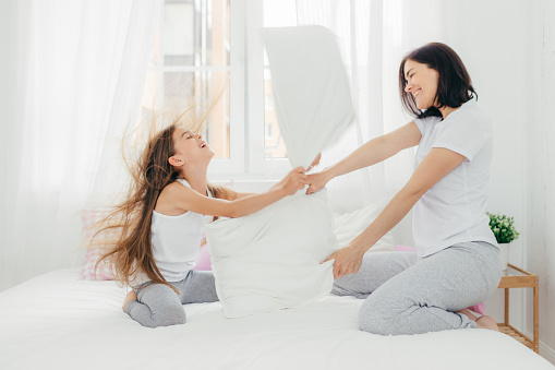 Joyous pillow fight between mother and daughter on a sunny day