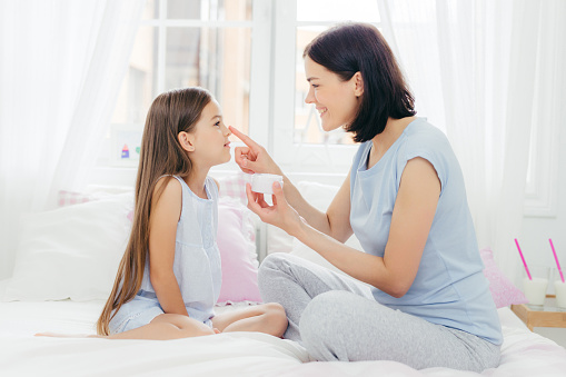 Mother applying cream on daughter's nose, shared skincare routine