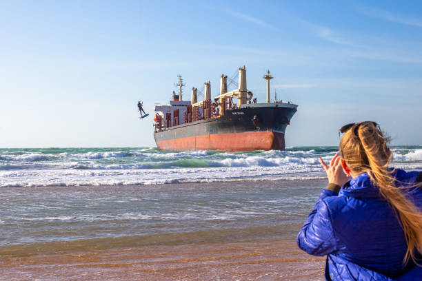 una mujer filma con su teléfono cómo un kitesurfista en una tabla vuela en el aire cerca de un gran barco en el mar. vityazevo, rusia - stranded men telephone beach fotografías e imágenes de stock