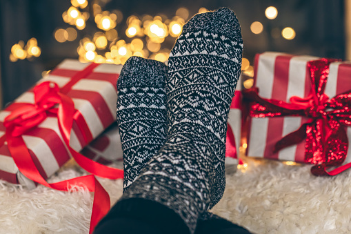 Feet in Christmas socks and gift boxes in front of the fireplace, close up, relaxing at home, cozy background.