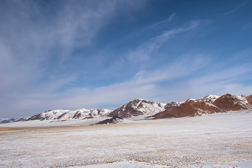 Snow mountain in Mongolia. Scenic landscape with snowy mountain top. Wonderful view from stony snowy mountain to mountain range under blue sky in sunny day.