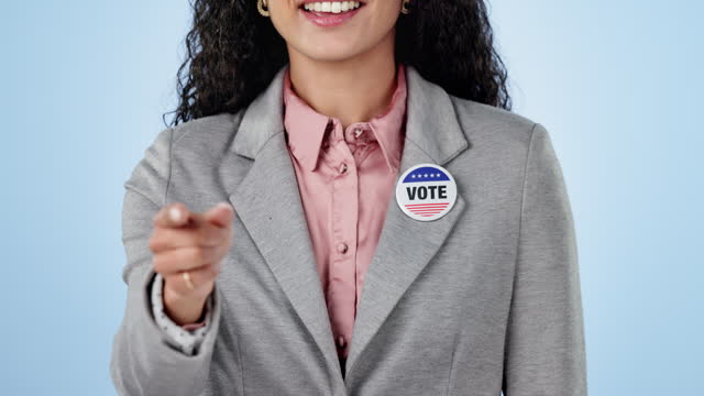 Woman in studio with pointing to vote, badge showing choice, okay and government party support. Politics, voting register or decision, politician with pin for campaign and election on blue background