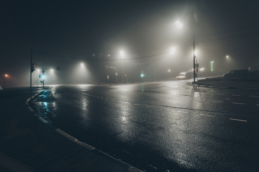 Foggy misty night road illuminated by street lights.