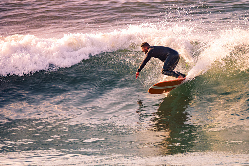 Surfing at Sunset. Young Man Riding Wave at Sunset. Outdoor Active Lifestyle.