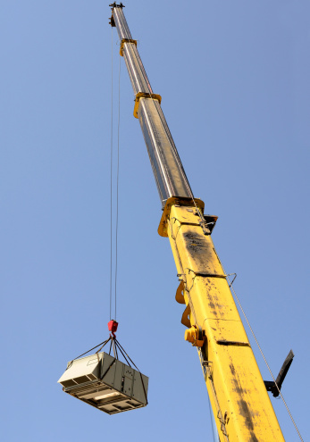 A large crane being used to remove a air conditioning unit from a commercial building