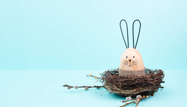 istock Easter bunny or rabbit sitting in a bird nest, willow branches, wooden egg, spring holiday, brown and blue color 1830780222