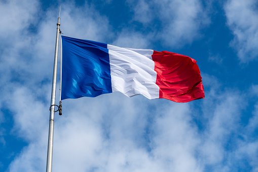 The French flag in the wind in front of a blue sky with veil clouds and a beautiful light. The flag has the color blue white and red