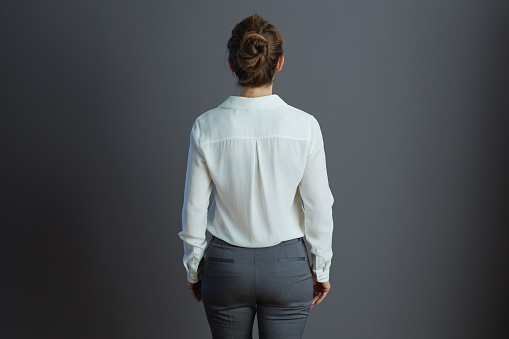 Seen from behind woman worker in white blouse isolated on gray.
