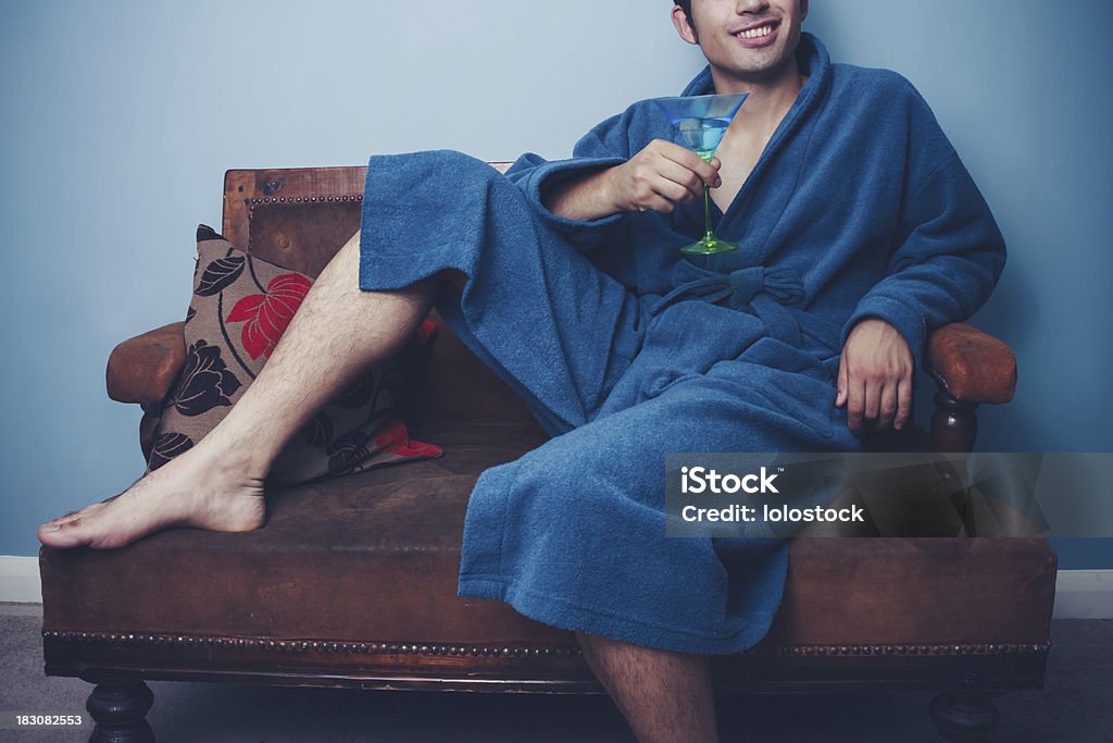 Felice giovane uomo in un vestito di medicazione bere cocktail - Foto stock royalty-free di Accappatoio