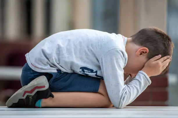 Photo of Crestfallen Crying child boy sitting at the schoolyard looking down