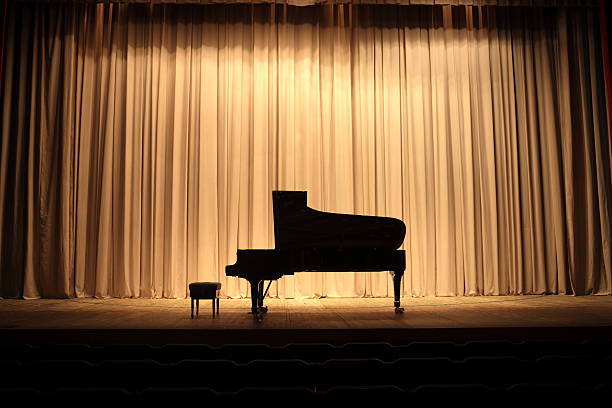 Placed center stage is the grand piano Grand piano at concert stage with brown curtain grand piano stock pictures, royalty-free photos & images