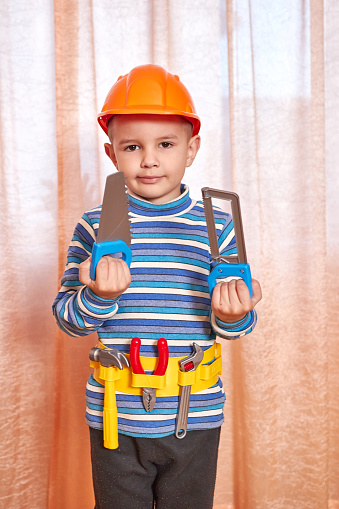 The boy is in a good mood with a toy helmet and tools.