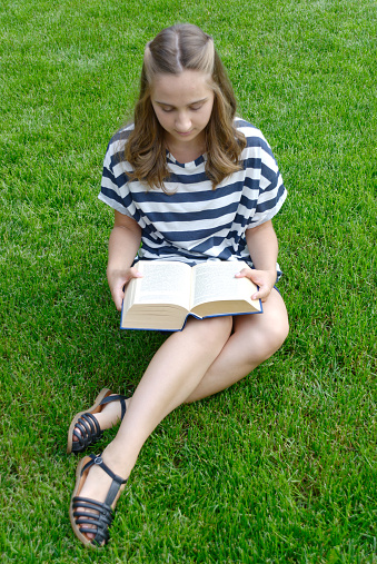 Beautiful young woman reading a book sitting on the green lawn