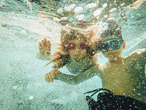 Child jumps to swimming pool and swims underwater, little active girl dives and has fun under water, healthy kids fitness and sport on family vacation