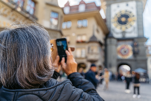 Senior woman taking a photo of the Zytglogge (Clock Tower) using her smartphone in Bern, Switzerland.
