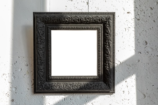 Vintage black frame with empty space to insert a painting, photo or other design on a white natural stone wall with shadows