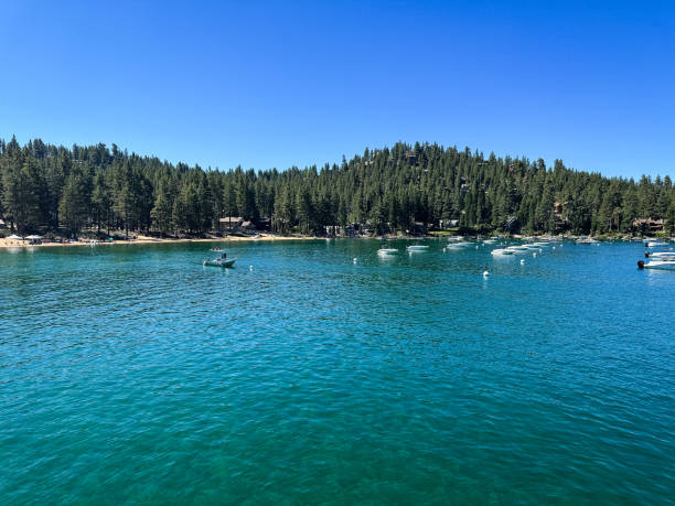 This scenic photograph captures a vibrant lakeside scene on iconic Lake Tahoe, featuring a bold red rescue boat gliding across sparkling turquoise waters. The boat is marked with \
