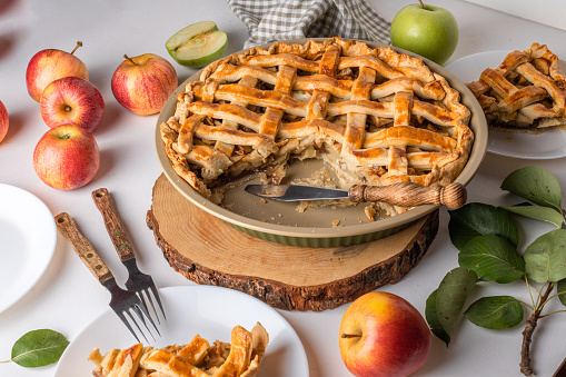 Homemade cutting Apple Pie with fresh apples on white kitchen table, ready to eat. Thanksgiving traditional dessert, Thanksgiving tart preparation, autumn bakery. Food Lifestyle, recipe