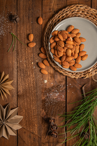 Almonds nuts on a plate placed on a rustic wooden board. Christmas background with pine branches tree and decoration on dark wooden board. Flat lay. Space for text