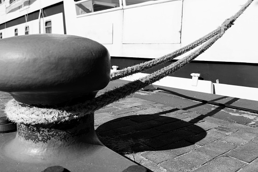 Iron mooring bollard with a rope and a ship at the harbor in black and white