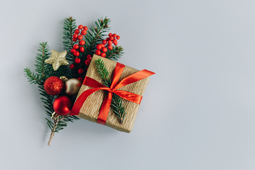 Gift box with spruce branches, Christmas ornaments and red berries on a red background. Holiday concept. Place for text.