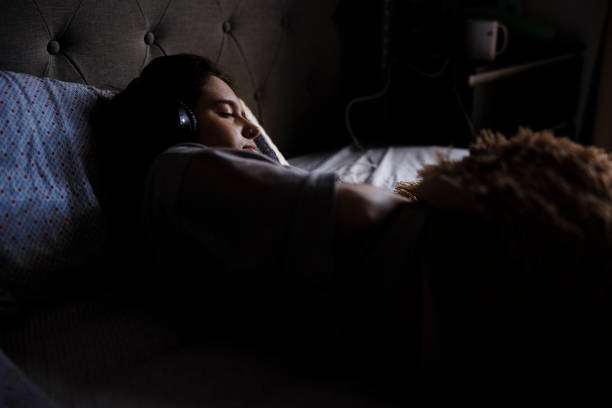 mulher burnout ouvindo música na cama, tentando meditar e dormir no quarto escuro - lying on side audio - fotografias e filmes do acervo