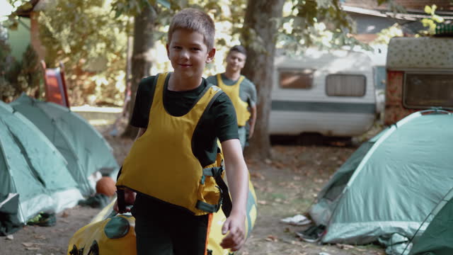 Teenagers in a life jacket at camp carry rubber kayaks ready to ride